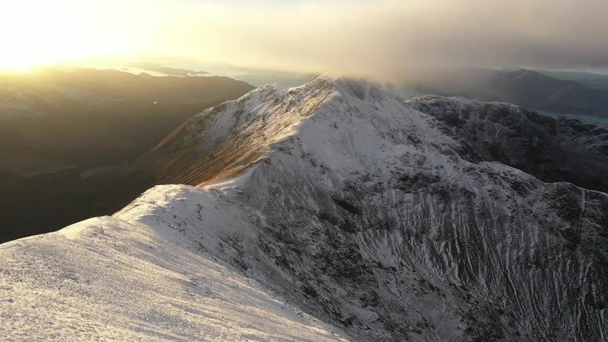 Sun shines across river onto snow covered mountain range on hazy day