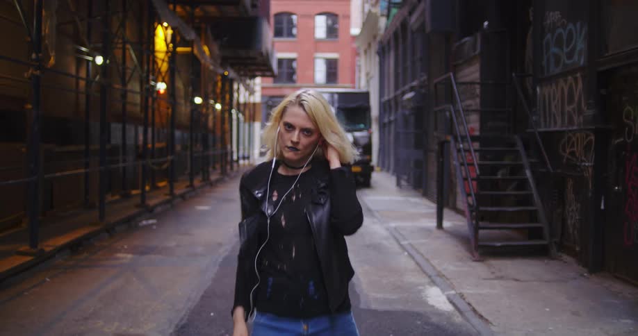 Woman climbs down stairs and stomps along alley before she starts dancing and making faces
