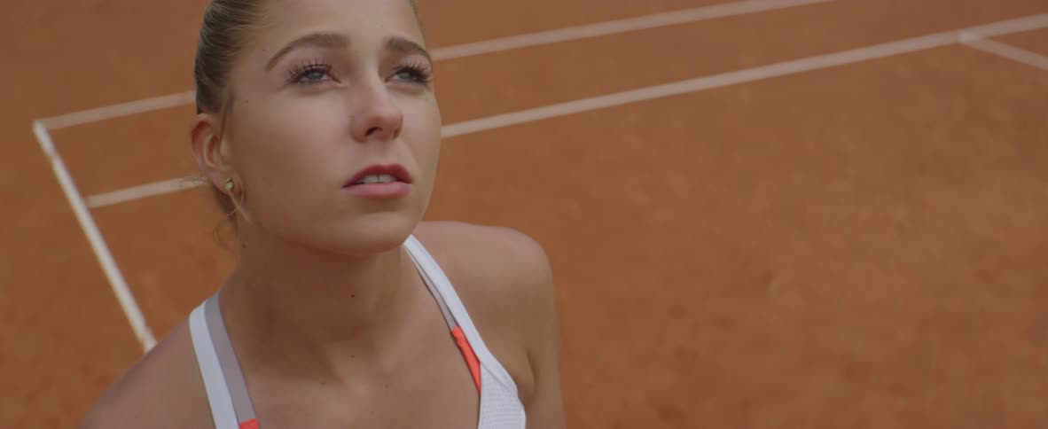Blonde female tennis player with ponytail looks around in tennis court