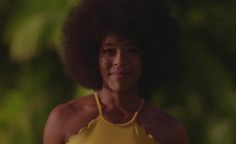 A young black woman stands outside and smiles