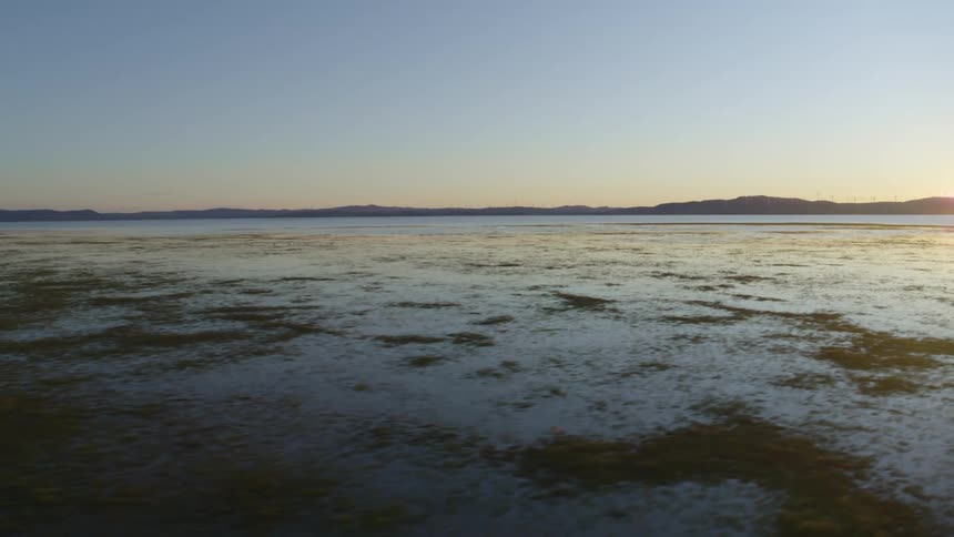 Sunlight reflects on the snow covered beach and there are mountains on the horizon