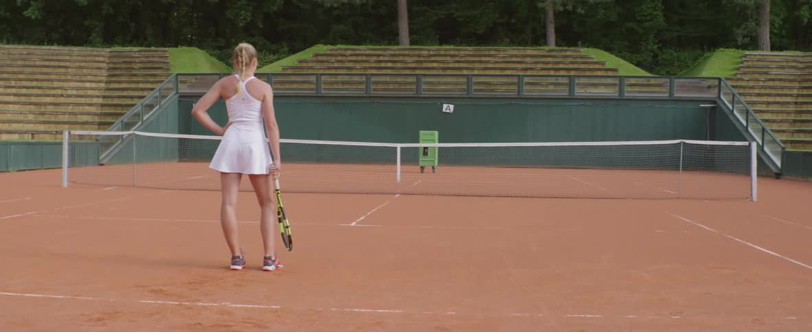 A tennis player stands on a court in an empty stadium
