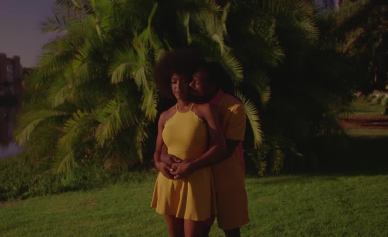 Couple stands in park near water cuddling