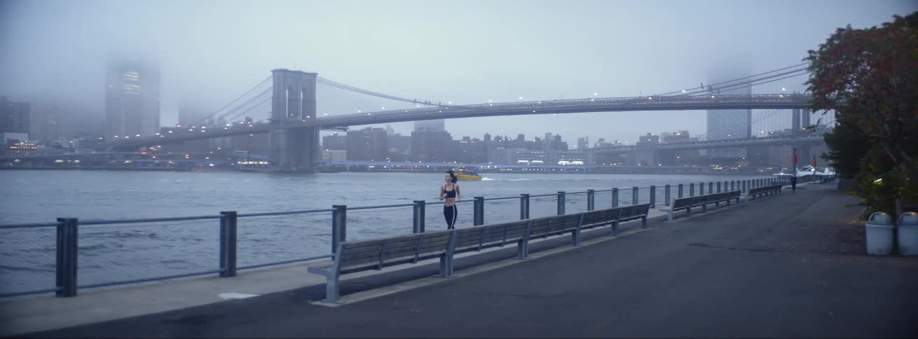 A woman runs along the riverfront as heavy traffic passes along a bridge behind her