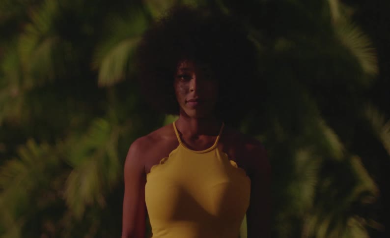 Young woman wearing a yellow dress looks at the camera standing in front of palm trees