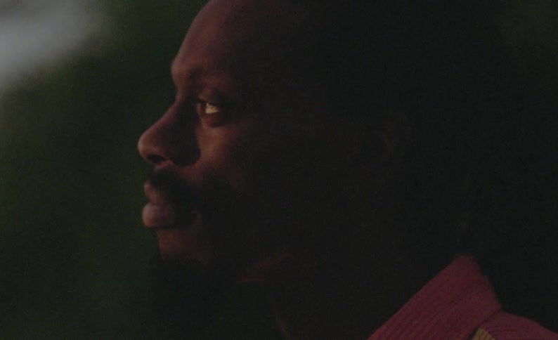 Side portrait of male dancer with braids and pink yellow shirt at dusk