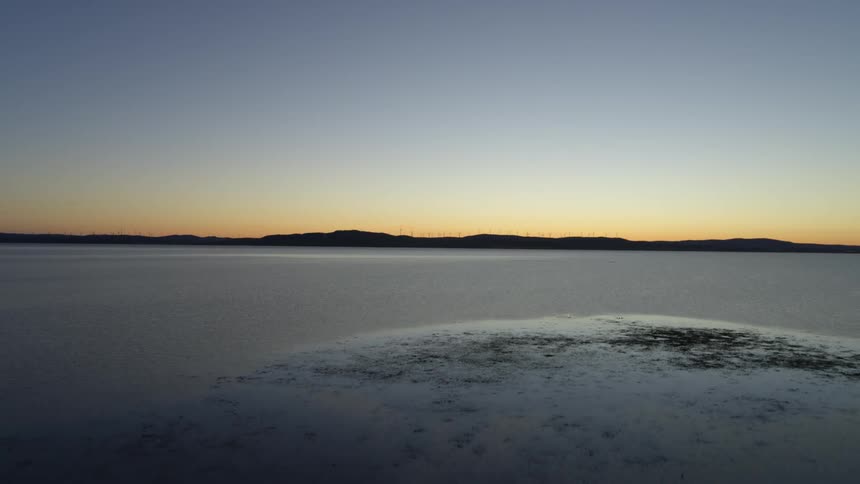 Snow on shore and mountains across the water on the horizon as the sun has set