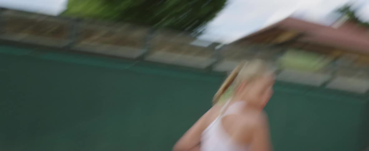 Blonde female tennis player with ponytail and white dress plays tennis in tennis court