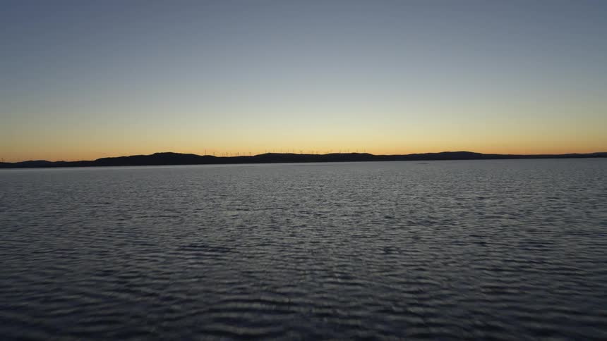 Aerial view moving across the water with mountains on the horizon as the sun has set