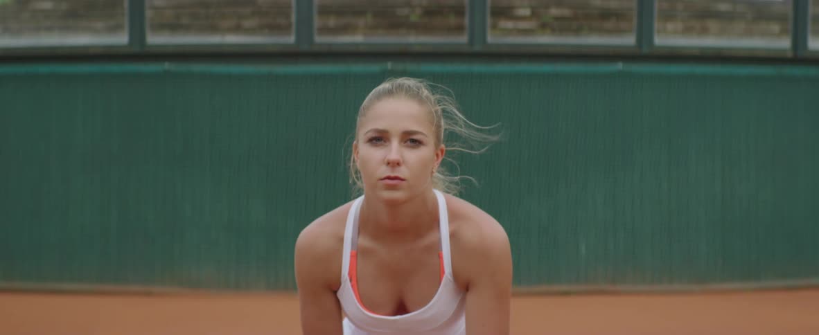 Blonde female tennis player with ponytail and white dress plays tennis in tennis court