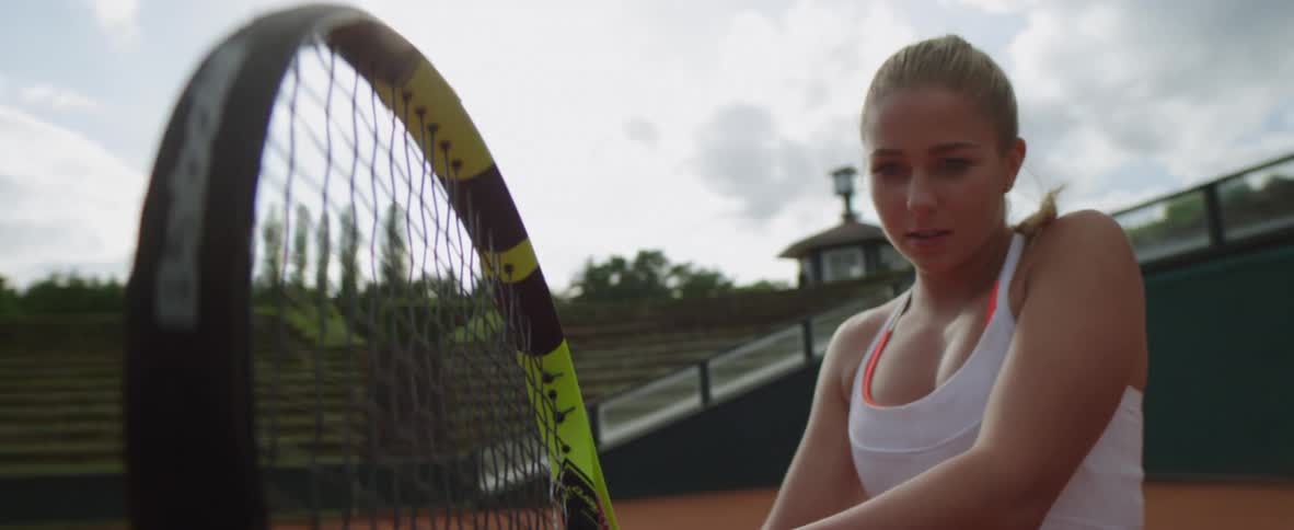 Blonde female tennis player with ponytail and white dress holds racket to play tennis in tennis court