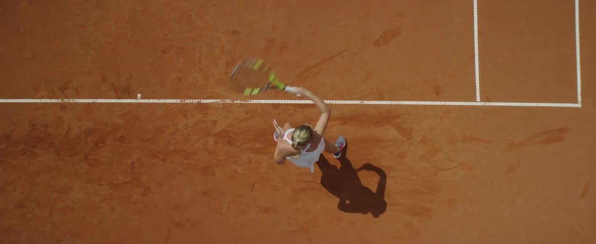Blonde female tennis player with ponytail and white dress plays tennis in tennis court