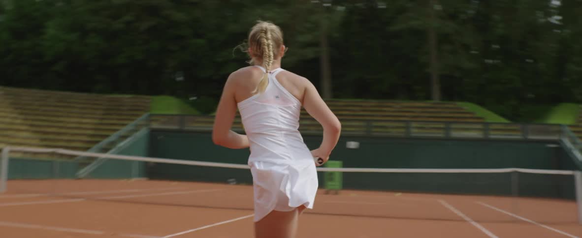 A female tennis player practices with an automatic machine on the court