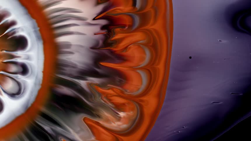 Orange and white paint expand in a circular shape against a purple background