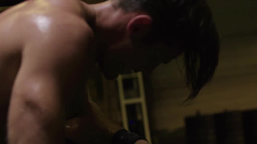 A shirtless man deadlifts and drops a weight then kneels in exhaustion