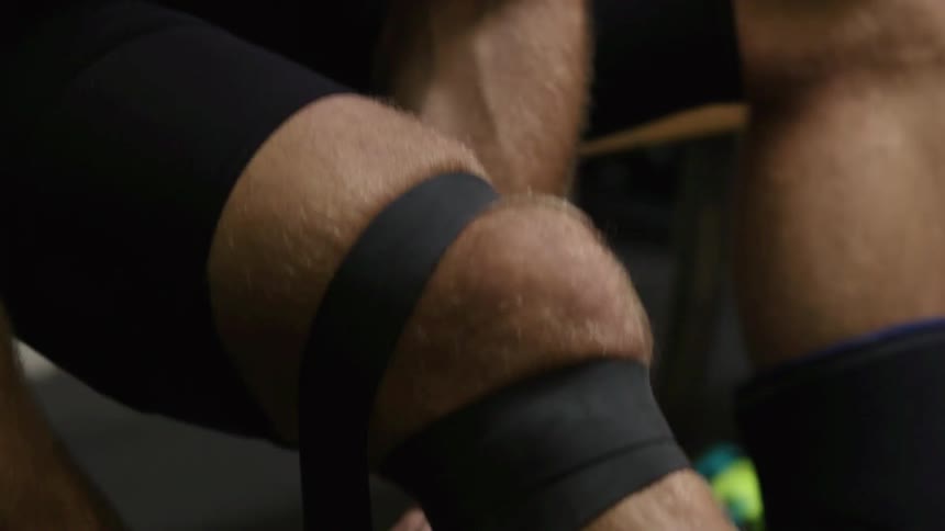 A man wraps his knee with sports-tape while sitting on a bench