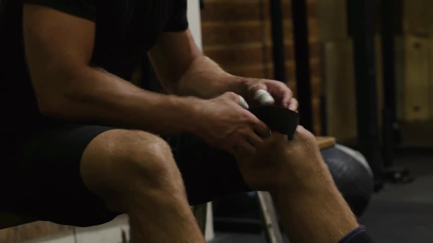 A man is taping his knee in a gym