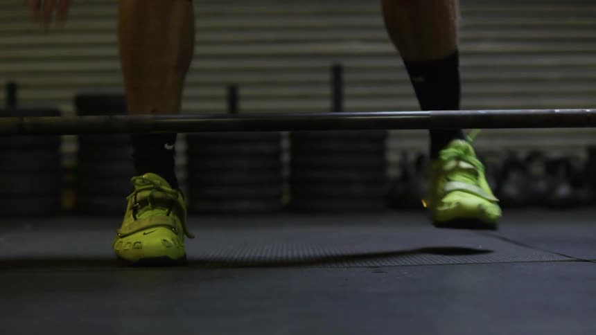 A person walks up to a weight bar, sets his feet and grips the bar