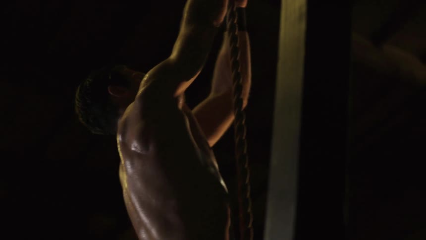 A shirtless man climbs up a rope