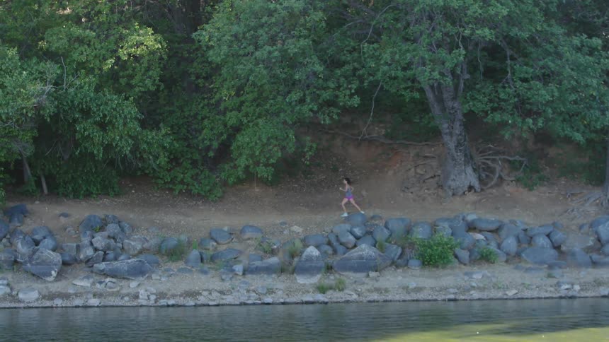 A woman jogging along a dirt path next to a rocky shoreline