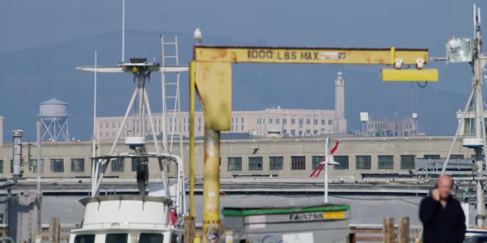 A crane on a pier near a docked boat as people walk and drive past on the street