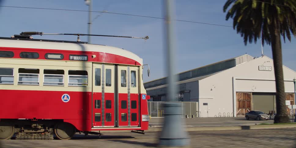 Overhead light rail travels along street passing buildings and pedestrians