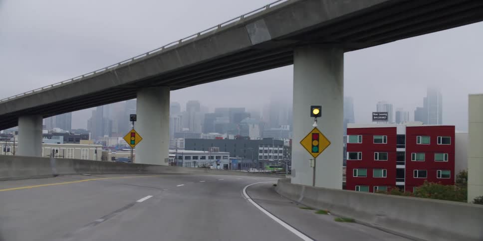 Vehicle driving on highway takes bend with high rise buildings in fog in the background