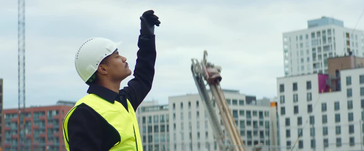 Male worker wearing safety vest and hard hat gives hand signals