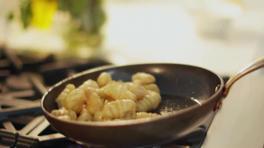 Gnocchi being cooked and tossed on a pan over a fire on the kitchen