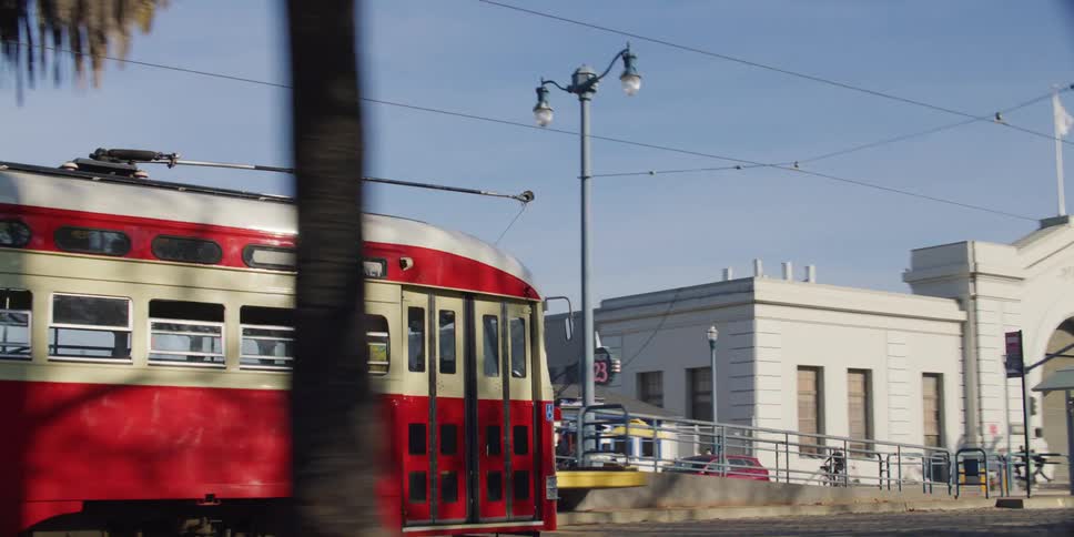 A person waits at a trolley stop as a red trolley approaches