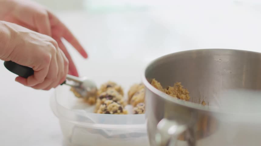 Woman with white red sweater takes cookie dough from pot using disher style scoop in the kitchen