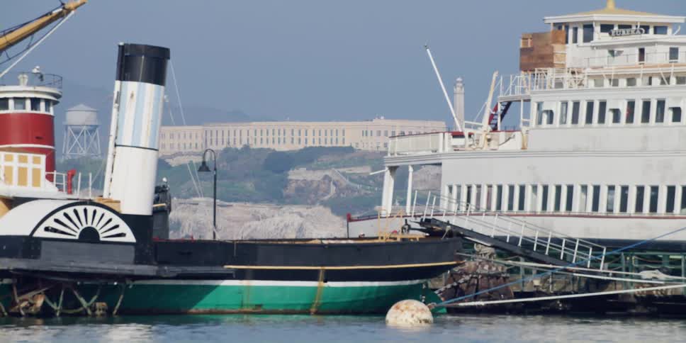Boat with a steam stack moves through water past building sitting on foggy shore