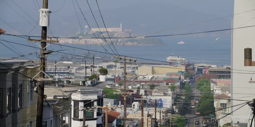 Hilly city street with poles and vehicles overlooking sea with small island