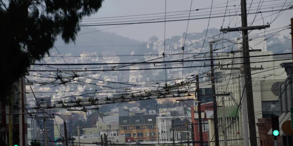 A neighborhood of homes on a hill with trolley wires hanging over the street