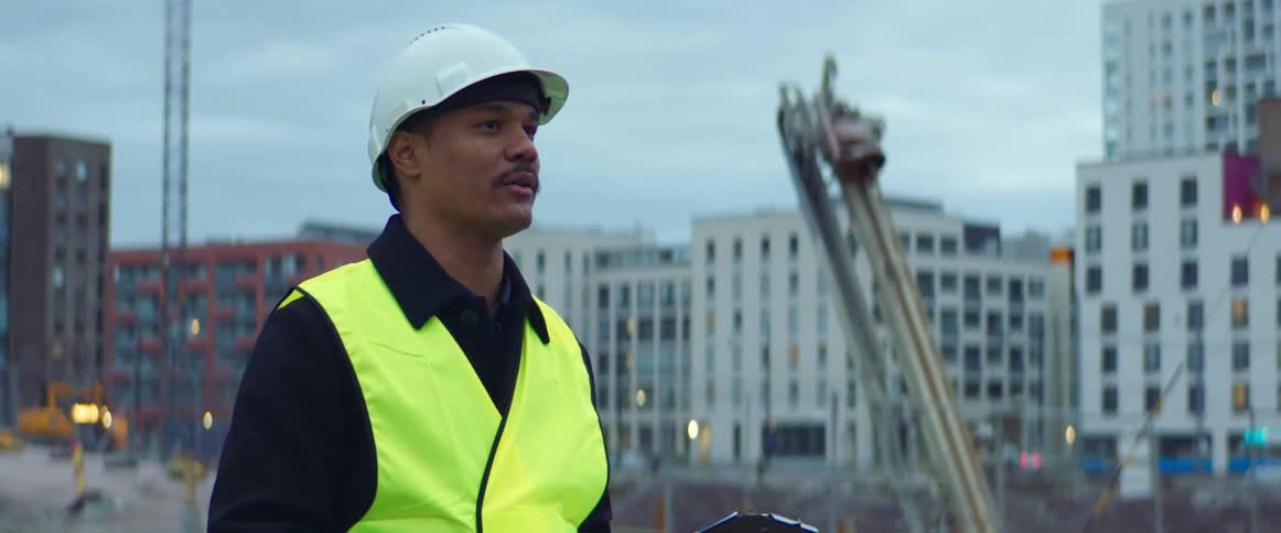Construction worker wearing a white hardhat and a yellow vest talking in a construction site