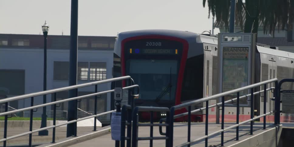 A subway pulls up to a station as people and a dog walk past