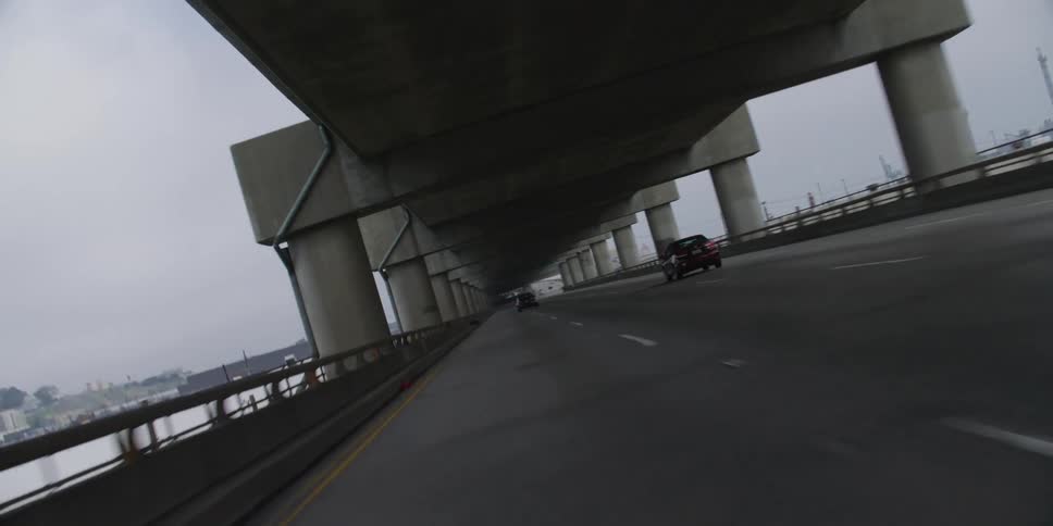 A vehicle speeds down a long bridge leading toward downtown