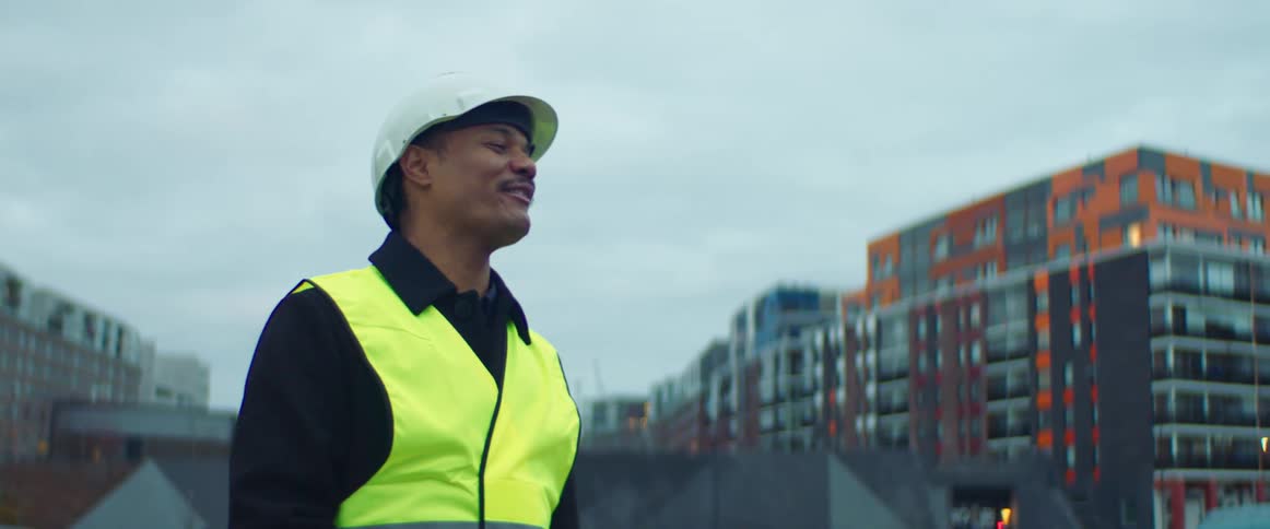 Construction worker wearing a white hardhat and a yellow vest talking in a construction site