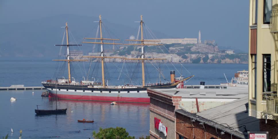 A large ship and a yacht sit in the sea outside a city neighborhood