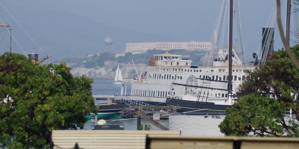 A man sitting on a bench overlooking the docked ferry and boats with alcatraz in view