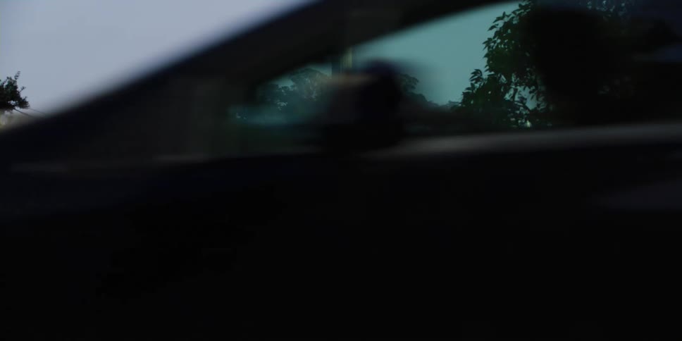 A vehicle drives down a road across from a neighborhood situated along a steep hill