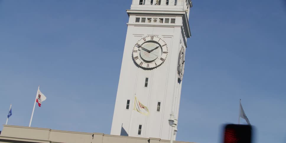 Flags are flying on a building near a clock tower under a clear blue sky