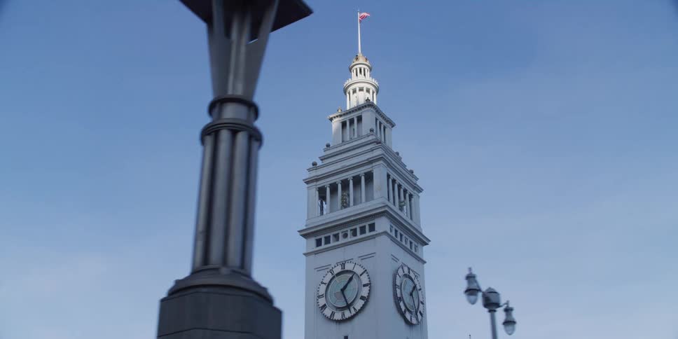 An american flag flies on top of a clock tower on a clear day