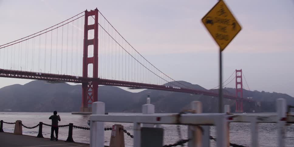 One person stands by the water near the large bridge
