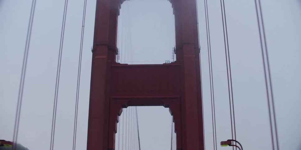 Automobiles are traveling across a suspension bridge and a view up to the cables above