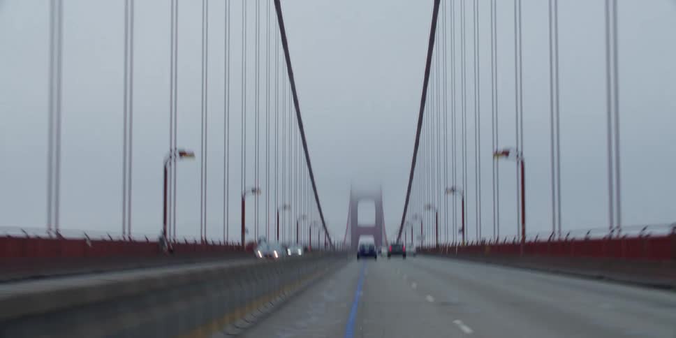 Vehicles speed across a bridge in heavy fog