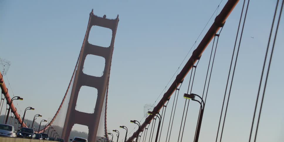 Twisting zooming footage of cars driving over the golden gate bridge at sunset