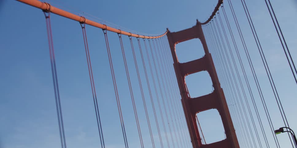 Automobiles are traveling across a suspension bridge and a view up to the cables above