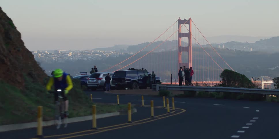 Cyclist rides through bike lane passing sightseers and their parked cars as they overlook fog covered san francisco and the golden gate bridge