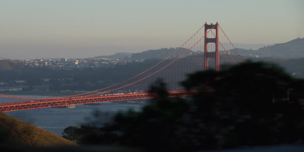 Traffic flows across suspension bridge on foggy day with city spreading to horizon in the background